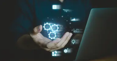 Mão segurando engrenagens digitais iluminadas na frente de um notebook, representando tecnologia e as ferramentas de apoio à inovação do MEI Tools.